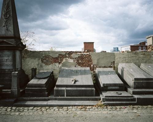 Vu de vieilles tombes en pierre et d'un mur défraichi sur fond scène urbaine, immeubles bâtiments et ciel contrasté, photographie argentique moyen format Plauble W67