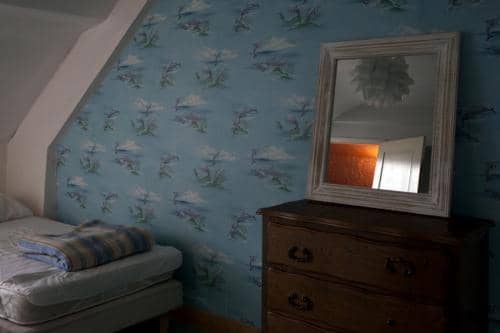 Une vieille chambre sous les combles aevc un vieux papier peint orné de dauphins, un vieux lit et de vieux meubles Dans la Creuse en France, à la Métive