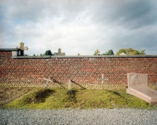 L'arrière d'un vieux cimetière à Lincent aevc des tombent d'anonymes et de simples croix en bois sur fonds de vieilles pierres et tombes, photographie argentique moyen format Plauble W67